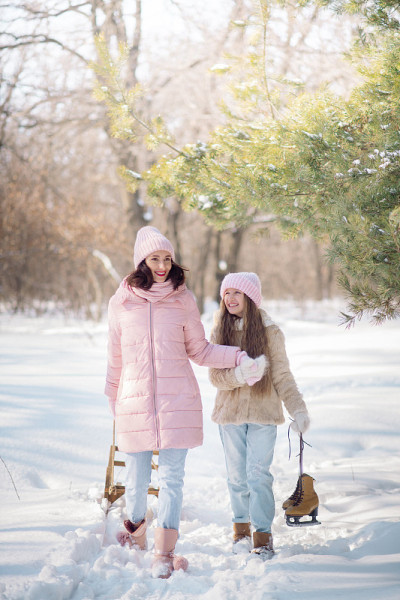 年轻的母亲和女儿在冰雪覆盖的冬天森林里散步