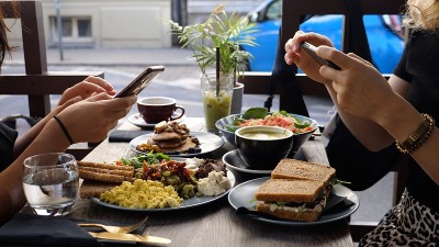 城市里的健康潮人午餐。两个美食博友正在用智能手机给他们的食物拍照