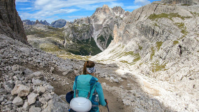 一名女子背着背包，拄着拐杖在意大利Dolomites的一条狭窄小路上徒步旅行。她周围有陡峭的山脉。很