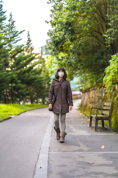 一个留着短发戴着面具的白人黑发女人在公园里散步。首次接触未受控制的Covid-19大流行
