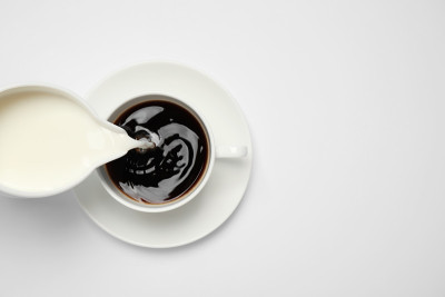 倒牛奶到咖啡杯的白色背景，俯视图
