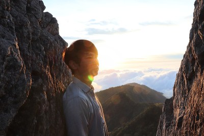 亚洲男人站在山顶看日落。