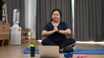 迷人的胖女人在家里用笔记本电脑练习瑜伽。