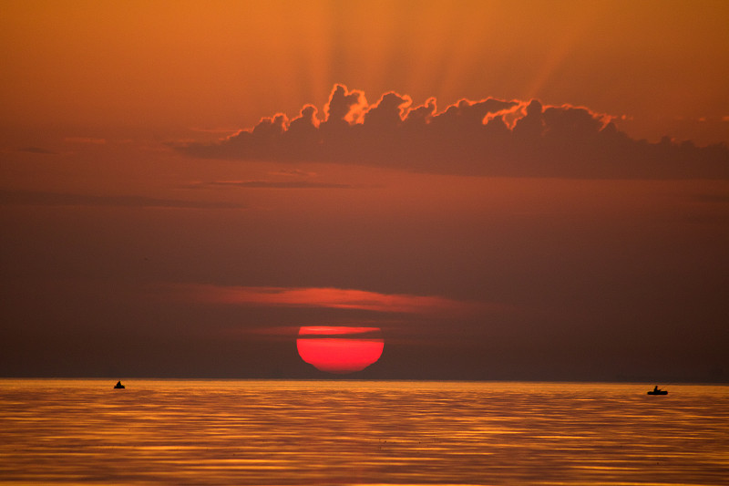 巨大的太阳在海平面上。日出时，水上有小船