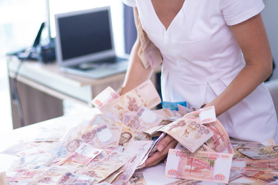 女性手中收集了很多钱在一张白色的桌子上，泰国钞票