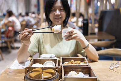 一位亚洲妇女正在用筷子夹起一种叫虾饺的广东点心
