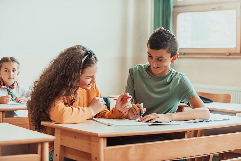 一个可爱的男孩和女孩坐在学校的课桌上一起工作。有选择性的重点