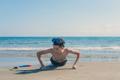 13岁的男孩在海滩上拧着潜水面罩和潜水管。旅游和夏季概念。
