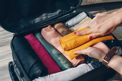 顶视图的女游客打开手提箱打包和安排彩色的衣服为旅行。