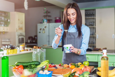 欢快的年轻女厨师烹饪甜点添加炼乳在菜在她的厨房