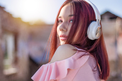 可爱的红发女士戴着耳机在夕阳下听着模糊的户外背景音乐