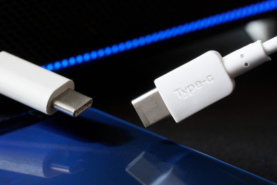 两个白色USB type-c连接器，旁边是一个蓝色智能手机和蓝色LED灯。现代技术和数据传输的概念。