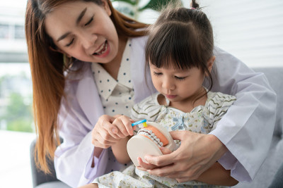 亚洲女牙医教可爱的小女孩用牙刷刷牙，口腔医生在牙科诊所告诉小女孩口腔卫生，教育和预防龋齿的概念。