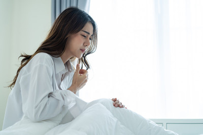 亚洲漂亮生病的女孩穿着睡衣从卧室里醒来。有吸引力的年轻女子感觉不好后醒来在床上和咳嗽在家里的清晨。健