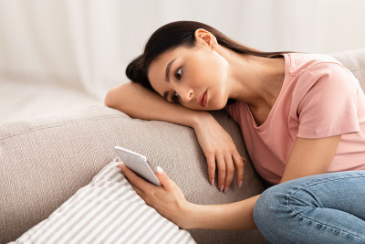 坐在沙发上看手机的沮丧女人