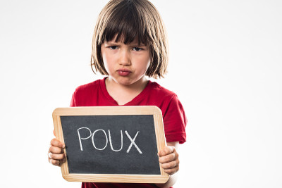 一个不幸的小女孩站在写着“poux”的学校石板后面
