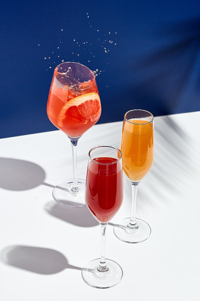 白色桌子，蓝色背景，Aperol饮料和贝里尼鸡尾酒。阳光和棕榈叶影饮现代静物。夏天，派对，热带和新鲜