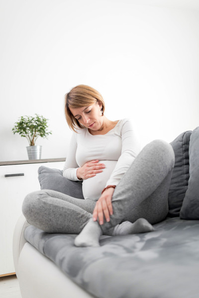怀孕疲惫不堪的女人带着肚子、腿和疼痛的问题躺在家里的沙发上，生病了。