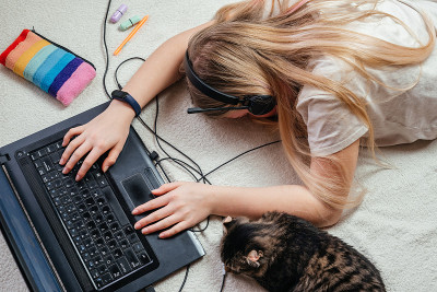 疲惫的少女戴着耳机睡在她的笔记本电脑和她的宠物猫
