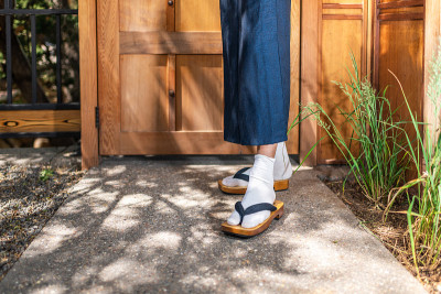 在日本户外花园中，穿着和服服装的男人脚上穿了一双tabi鞋和袜子，由木制的现代现代门组成