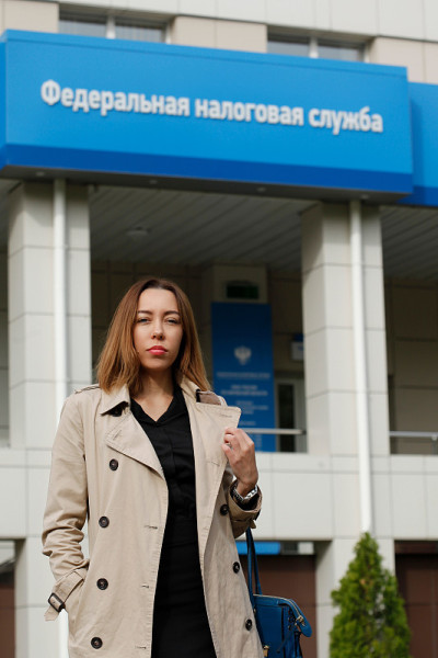 迷人的俄罗斯女人站在美国国税局大楼前(俄罗斯)看着镜头。俄文题词-国税局