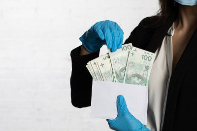 女商人戴着防护面具和防护手套，把一捆纸币放进信封里。