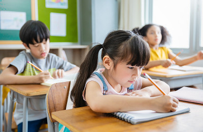 小学生在教室课桌上写字的肖像。在小学做测验的女学生。孩子们在教室里写笔记。教育知识观