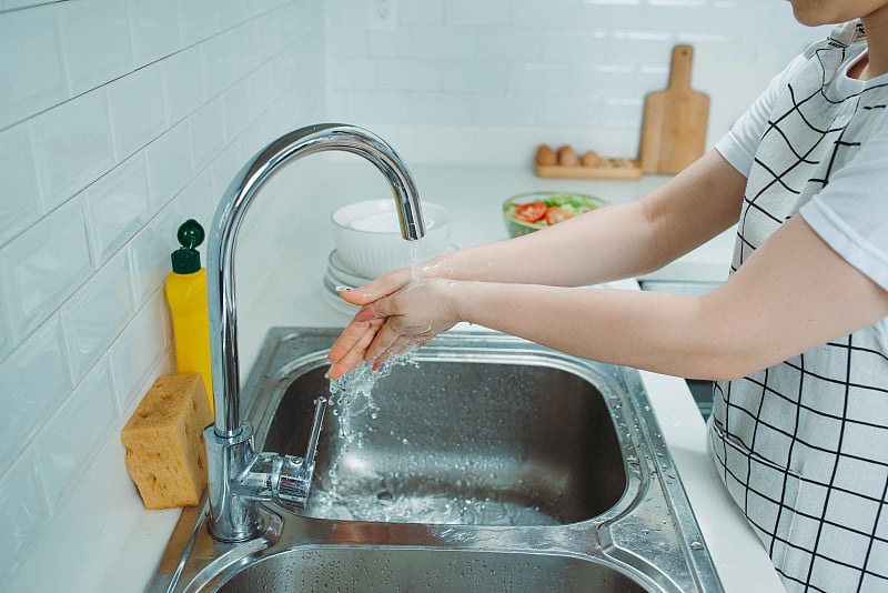 迷人的年轻女子正在洗碗，同时在家里打扫卫生