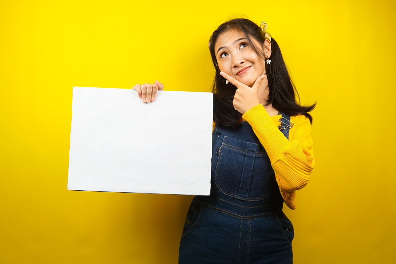 漂亮可爱的年轻女子在思考，手握空白的空横幅、标牌、白板、空白招牌、白色广告牌，在文案空间展示东西，促