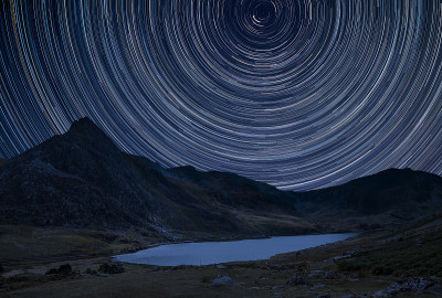 北极星周围的星迹数字合成图像和斯诺登尼亚的Llyn Ogwen周围的乡村景观图像