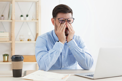 疲惫的商人穿着蓝色衬衫在办公室工作，用手指触摸紧闭的眼睛，试图克服压力和疲惫，想睡觉