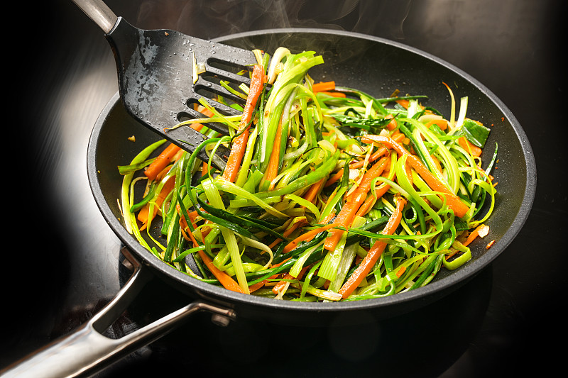 用胡萝卜丝和青葱条在黑色煎锅里煮健康的蔬菜面条，这是一种素食餐