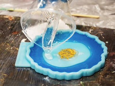 将环氧树脂倒入金色玩具的艺术过程。树脂艺术风格的绘画工艺，在工作室用环氧树脂创作，用图像做一个木架。