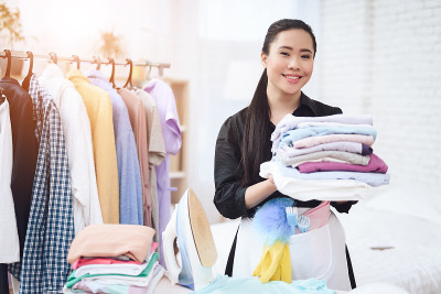 年轻的亚洲女佣把熨好的衣服放在更衣室。熨烫衣服。