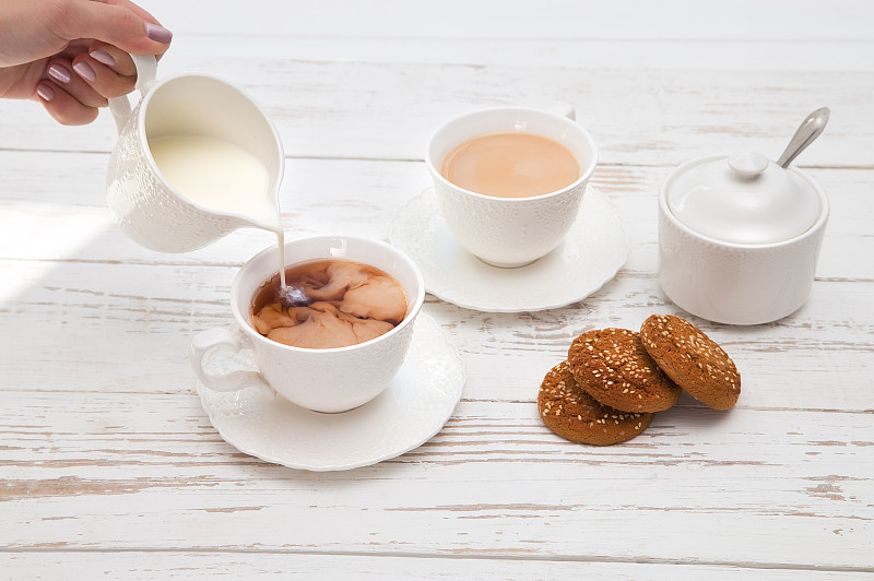 双手将奶油倒进白色木桌上的茶杯里
