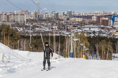 一名穿着滑雪服、面带微笑的男子在积雪覆盖的斜坡上用拖曳式电梯滑雪。