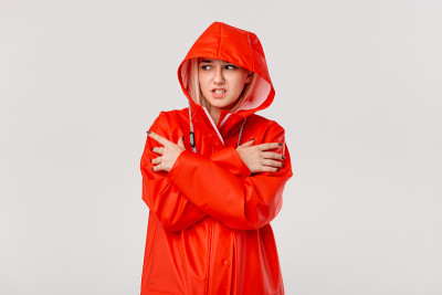 金发女孩穿着红色雨衣，戴着兜帽，站在白色的背景下孤立无援。你准备好迎接寒冷的坏天气了吗?