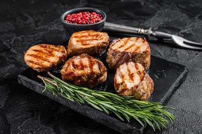烧烤烤猪肉圆片牛排，里脊肉。黑色背景。俯视图