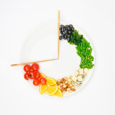 五颜六色的食物和筷子排列成一个时钟的形式在盘子上。间歇性禁食、节食、减肥、午餐时间观念。