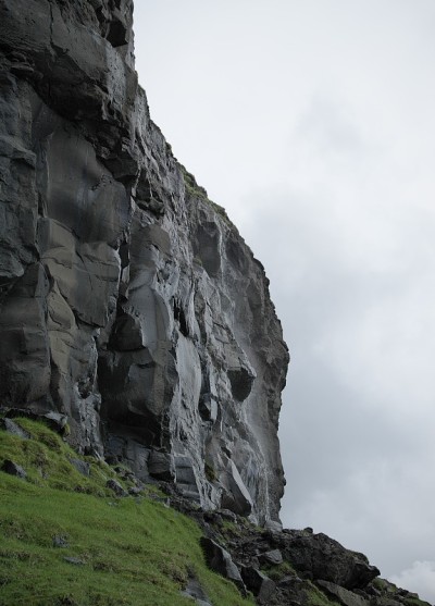 在法罗群岛的Vagar岛的火山起源的湿黑色岩石墙的景观图像。