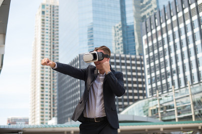 白人商人穿着黑色西装和虚拟现实头盔(VR)，并以拳头打到空中