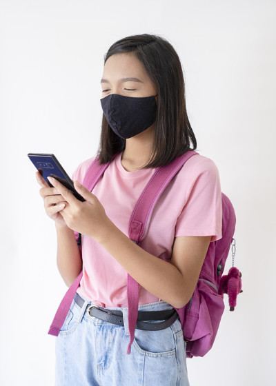 亚洲年轻女孩戴着面具使用手机在白色背景。