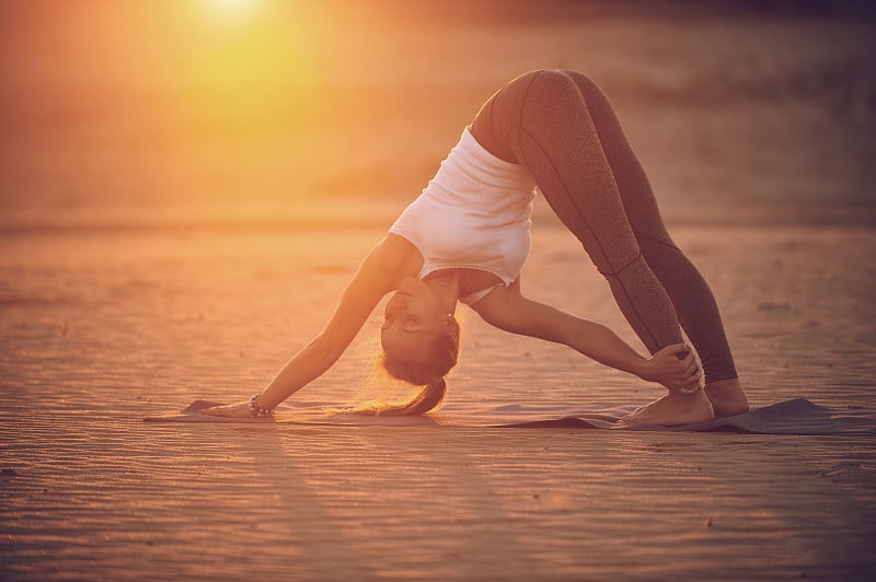 美丽的年轻女子练习瑜伽体式Adho Mukha Svanasana -在沙漠日落下狗