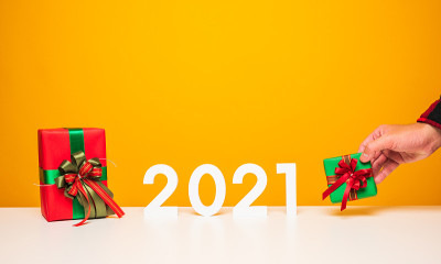 圣诞快乐，新年快乐2021白色桌子和黄色背景与男性手拿起礼物盒的模型。