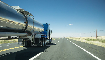 在高速公路上，一辆带银色油箱拖车的卡车经过一辆轿车