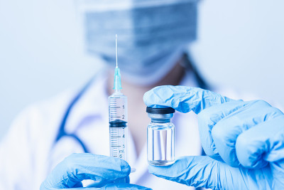 女医生带听诊器戴面罩，在实验室里拿着注射器和药瓶接种疫苗