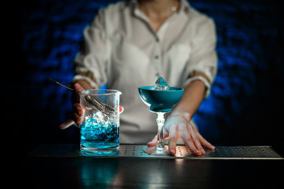 调酒师的手放在吧台上的蓝色杯子和调酒杯上的蓝色冷鸡尾酒
