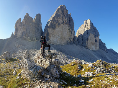 一名男子站在一块巨石上，欣赏意大利Dolomites地区的Drei Zinnen山的近景。尖锐而高大