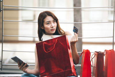 年轻的亚洲成年妇女拿着信用卡和购物袋。