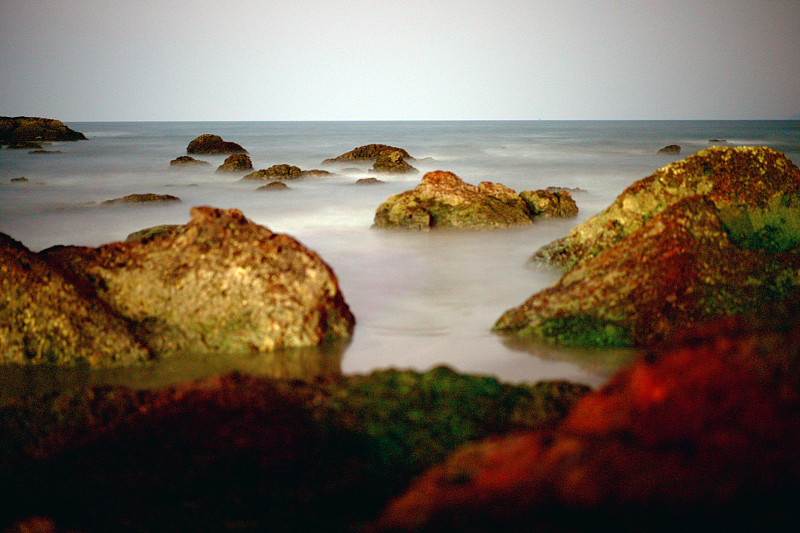 岩石海滩风景。白色浪花溅在石头上。夜潮。晚上海浪翻滚。晚上海滩。